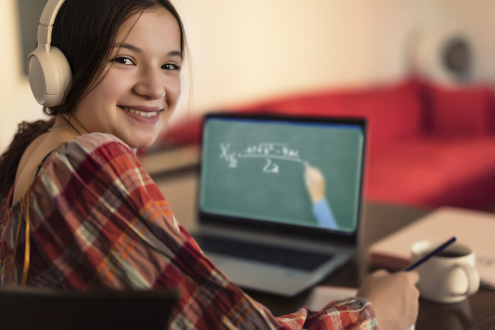 Secondary school aged girl looking back over her shoulder at the camera, with a laptop on her lap