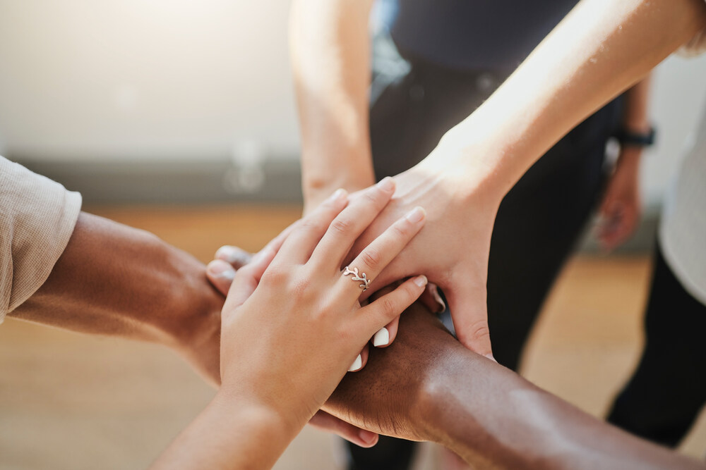 Hands of 4 people all on top of each other in the middle