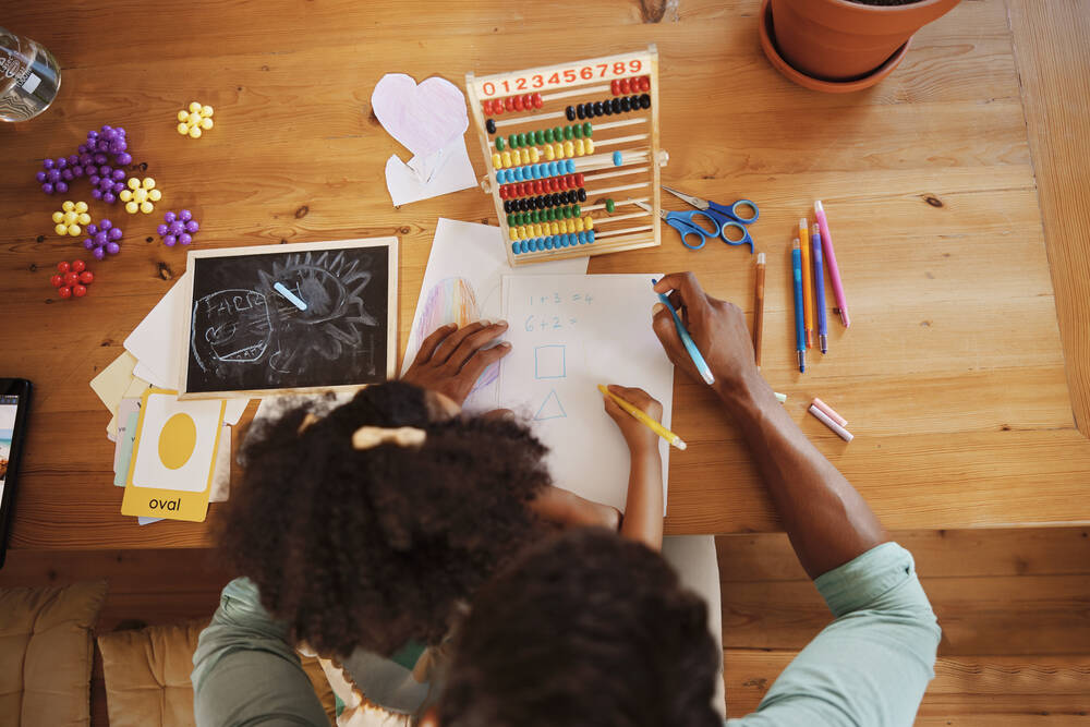 Overhead photo of girl and adult doing maths on a wooden desk