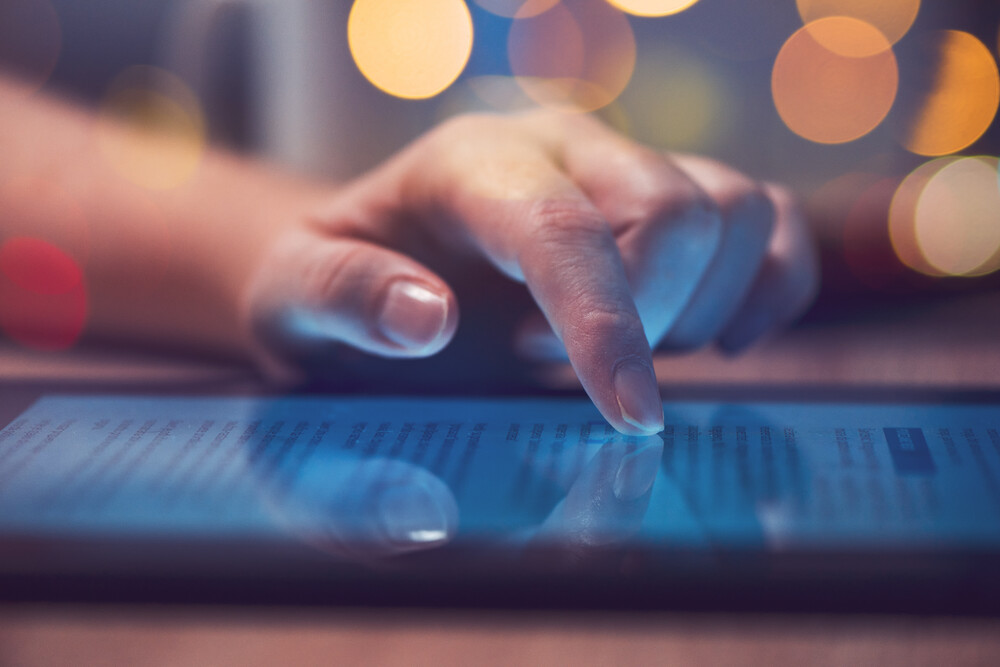 Hand touching the screen of a tablet or similar device on a table